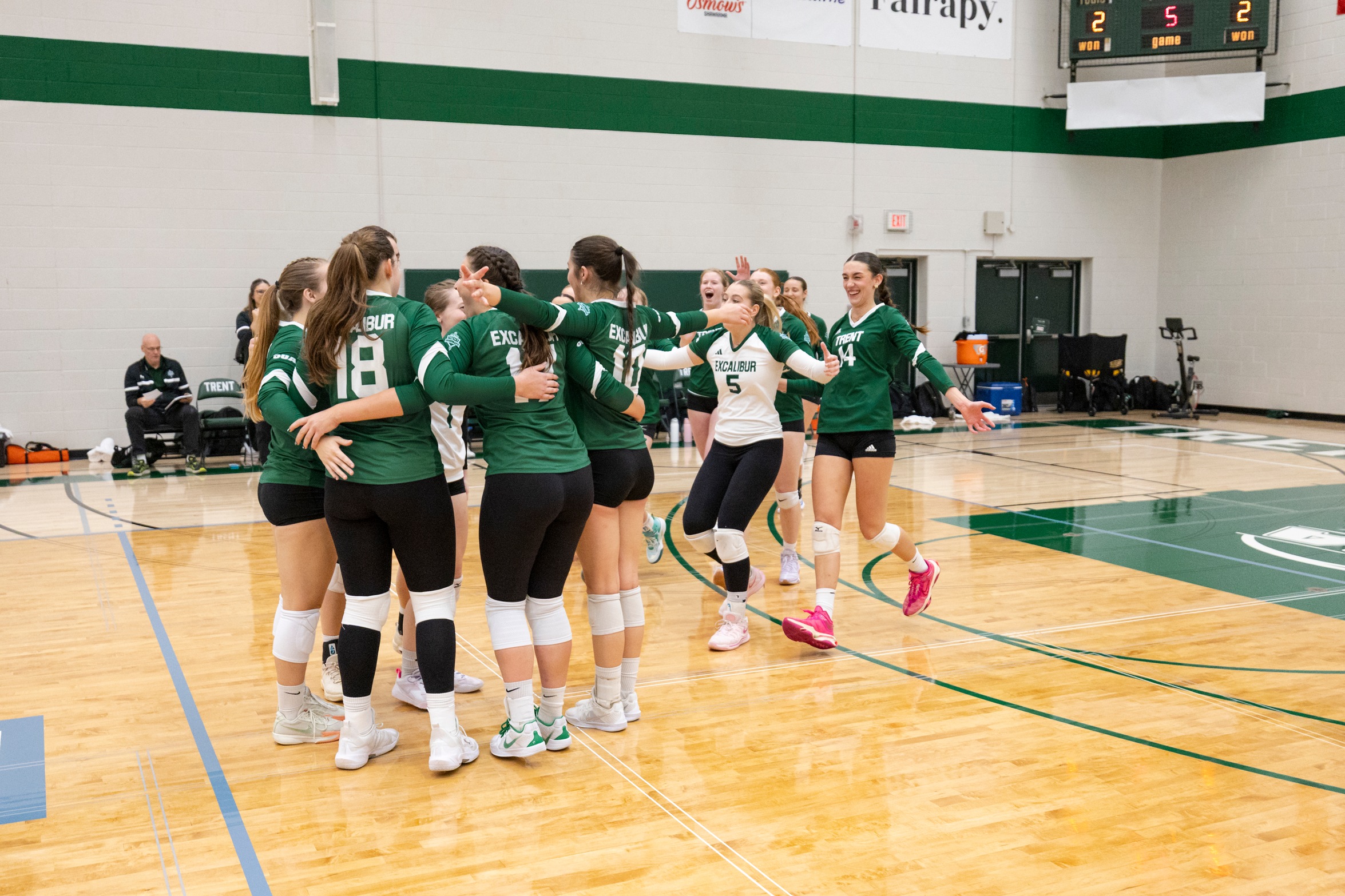 members of the women's volleyball team huddle and cheer mid game