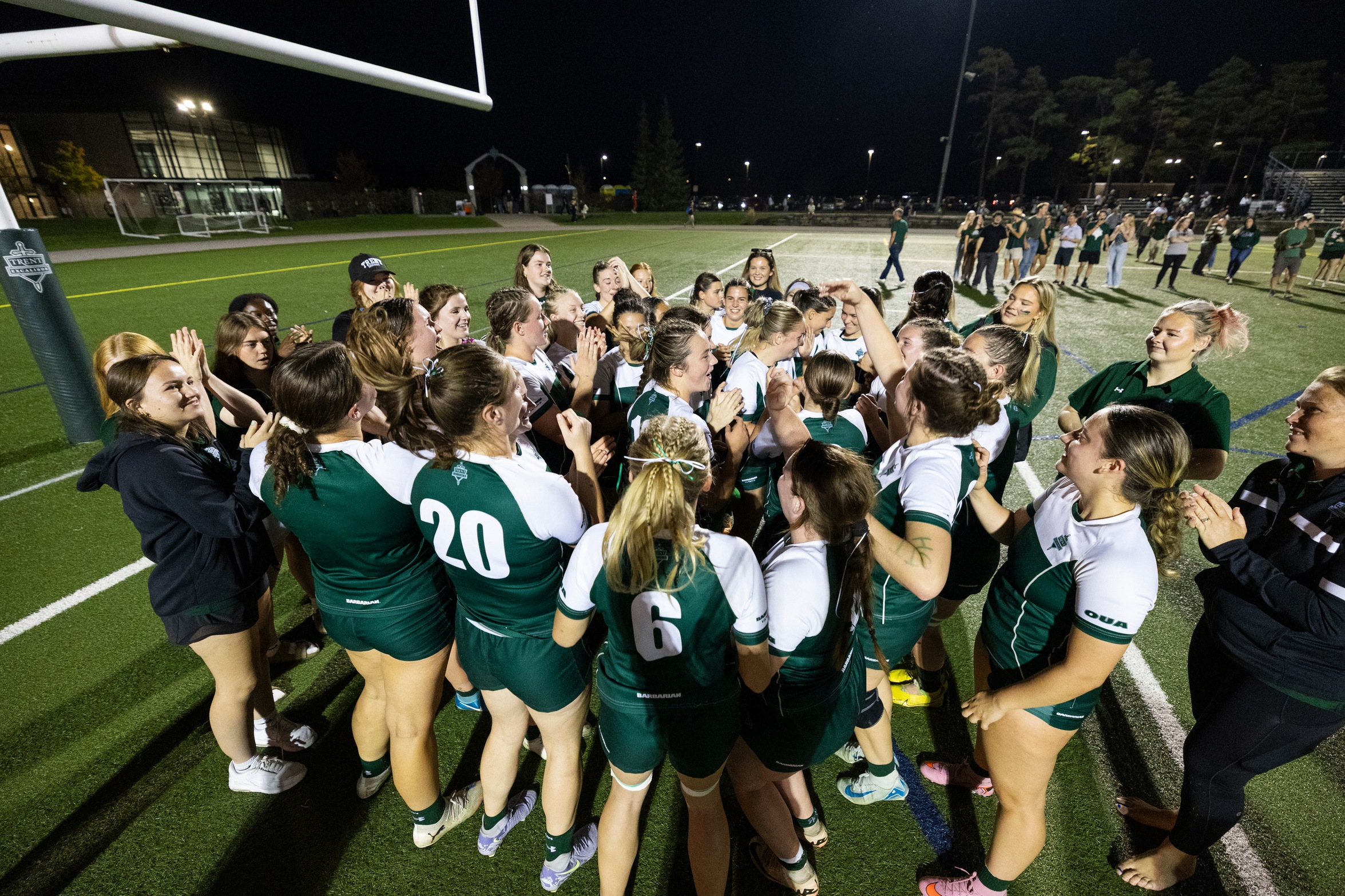 Excalibur women's rugby team in a large huddle, celebrating their 2025 victory over Waterloo.